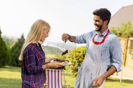Photo for Couple making a backyard barbecue party on a sunny summer day, grilling meat and having fun - Royalty Free Image