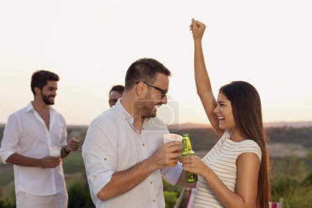 Foto de Pareja enamorada divirtiéndose en una fiesta de verano al aire libre, bailando y bebiendo cerveza - Imagen libre de derechos