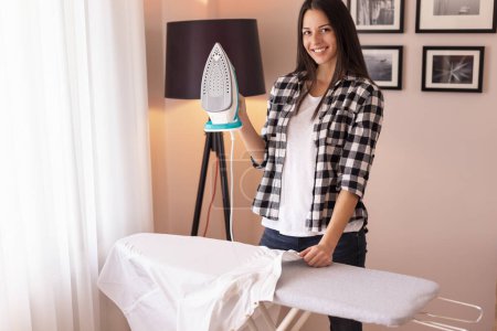 Photo for Woman holding the iron, ironing washed, wrinkled clothes on the ironing board - Royalty Free Image
