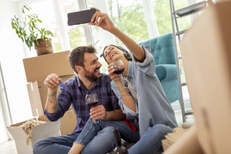 Photo for Young couple in love moving in new apartment, drinking wine and having fun taking selfies with apartment keys - Royalty Free Image