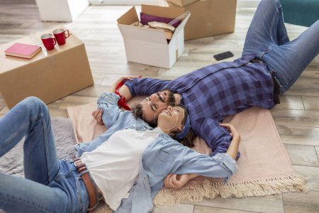 Téléchargez les photos : Vue grand angle de beau jeune couple amoureux couché à l'envers sur le sol de leur nouvelle maison et relaxant, prenant une pause tout en emménageant ensemble - en image libre de droit