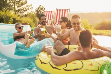 Téléchargez les photos : Groupe d'amis à une fête d'été au bord de la piscine, s'amuser dans la piscine, boire des cocktails et de la bière et porter un toast - en image libre de droit