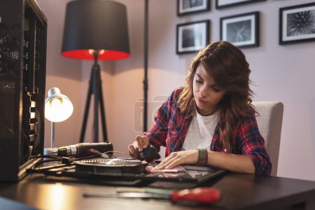 Téléchargez les photos : Jeune femme effectuant un entretien informatique, éliminant la poussière des composants - en image libre de droit