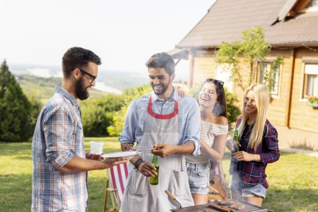 Photo for Group of friends making barbecue in the backyard, drinking beer and having fun on a sunny summer day - Royalty Free Image