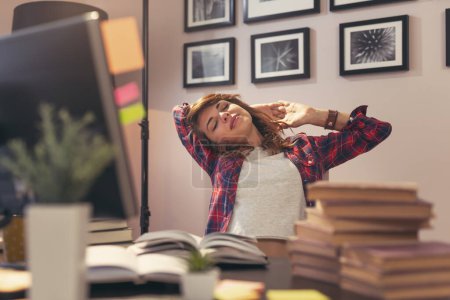 Foto de Mujer cansada sentada en un escritorio en su oficina y estirándose, estudiando para un examen - Imagen libre de derechos