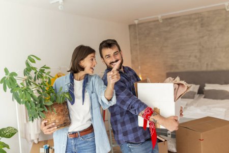 Photo for Couple in love moving in together, having fun while carrying cardboard boxes with their stuff and setting up the new apartment - Royalty Free Image