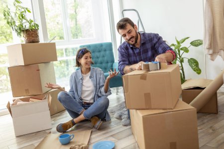Photo for High angle view of a young couple in love sitting on the floor of their apartment, packing things into cardboard boxes, getting ready for relocation - Royalty Free Image