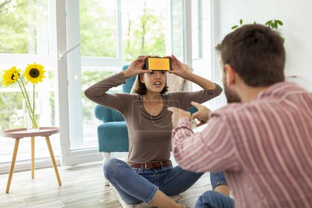 Photo for Couple having fun at home playing charades, explaining and guessing the words from a smartphone app - Royalty Free Image
