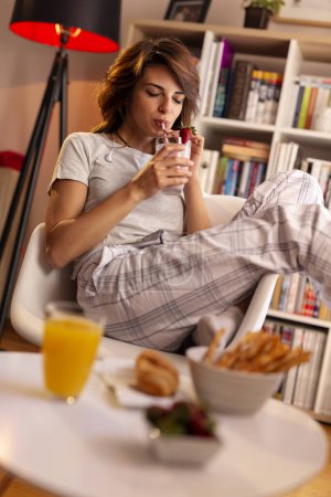 Photo for Beautiful young woman enjoying weekend morning, having breakfast and drinking a fresh strawberry smoothie - Royalty Free Image