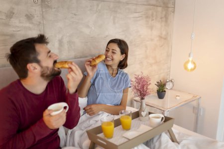Téléchargez les photos : Beau jeune couple amoureux couché au lit, se détendre le matin et prendre le petit déjeuner - en image libre de droit