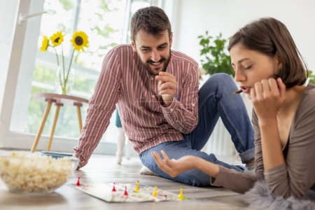 Photo for Couple in love enjoying their time together, eating popcorn and having fun while playing ludo board game - Royalty Free Image