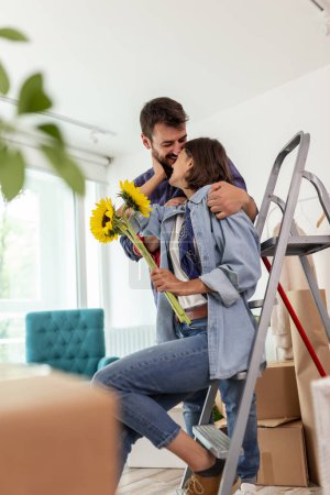 Téléchargez les photos : Couple emménageant ensemble dans un nouvel appartement, mari femme surprenante avec un bouquet de fleurs - en image libre de droit