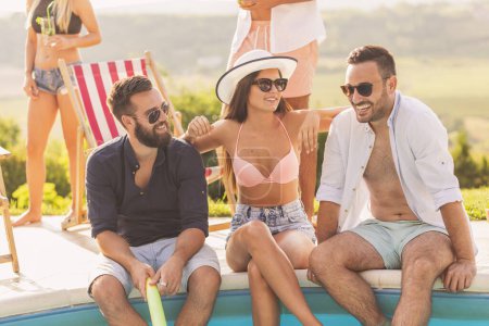 Téléchargez les photos : Groupe d'amis à une fête d'été au bord de la piscine, assis au bord d'une piscine, boire des cocktails et s'amuser - en image libre de droit