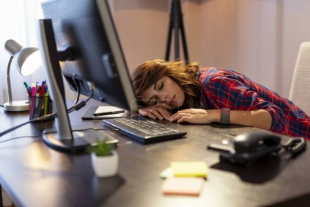 Photo for Young woman exhausted because of working overtime, asleep at desk at her home office - Royalty Free Image