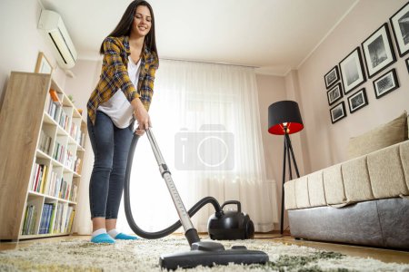 Foto de Mujer joven haciendo tareas domésticas, aspirando la alfombra de la sala de estar - Imagen libre de derechos
