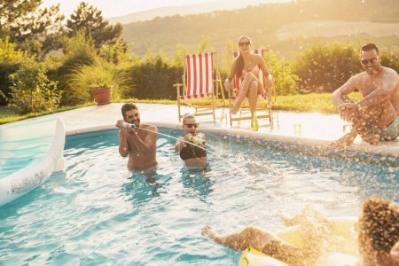 Téléchargez les photos : Groupe d'amis à une fête d'été au bord de la piscine, s'amuser dans la piscine, boire de la bière et éclabousser de l'eau - en image libre de droit