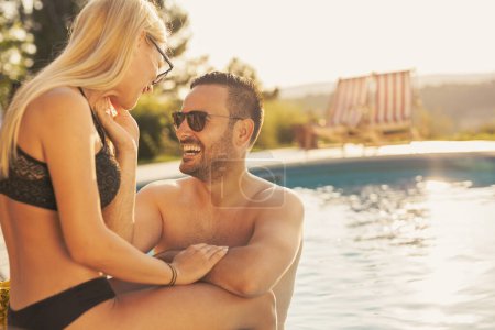 Téléchargez les photos : Couple amoureux à une fête d'été au bord de la piscine, assis au bord d'une piscine, bronzer, boire des cocktails et s'amuser - en image libre de droit