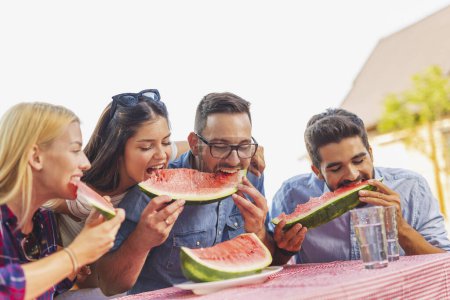 Photo for Group of friends having an outdoor lunch, eating fresh watermelon slices and having fun - Royalty Free Image