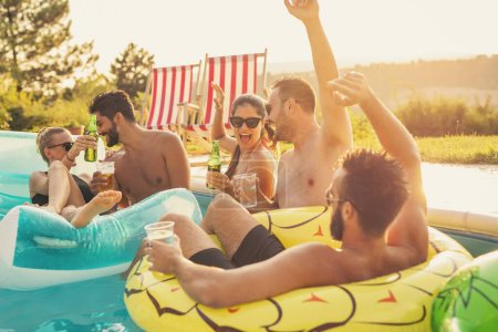 Foto de Grupo de amigos en una fiesta de verano junto a la piscina, divertirse en la piscina, bailar, beber cócteles y cerveza y hacer un brindis - Imagen libre de derechos
