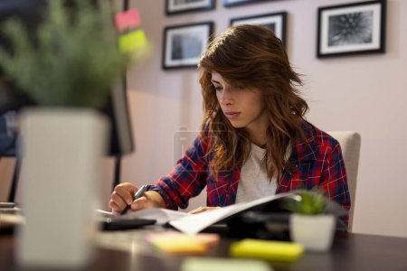 Téléchargez les photos : Jeune femme travaillant dans un bureau à domicile, signant un contrat. Focus sur le visage et la main - en image libre de droit