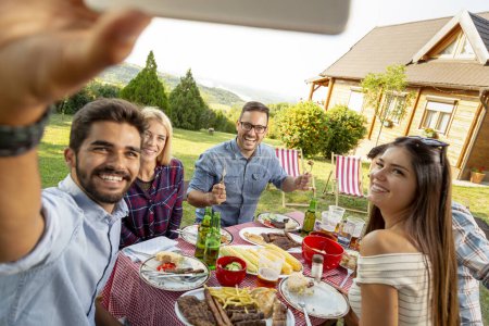 Téléchargez les photos : Groupe d'amis faisant une fête barbecue dans la cour, mangeant le déjeuner à l'extérieur et s'amusant à prendre des selfies - en image libre de droit