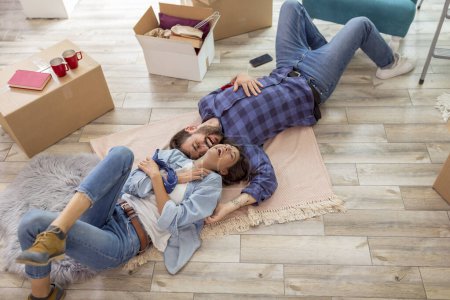 Téléchargez les photos : Vue grand angle de beau jeune couple amoureux couché sur le sol de leur nouvelle maison à l'envers et relaxant, prenant une pause tout en emménageant ensemble - en image libre de droit