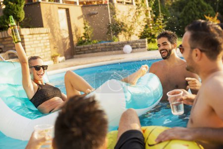 Foto de Grupo de amigos en una fiesta de verano junto a la piscina, divirtiéndose en la piscina, bebiendo cócteles y cerveza y haciendo un brindis - Imagen libre de derechos