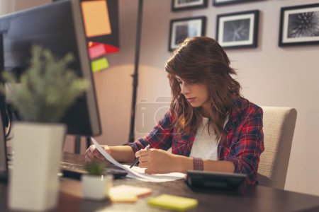 Foto de Mujer joven revisando documentos, trabajando hasta tarde en una oficina en casa - Imagen libre de derechos