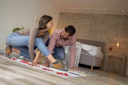Photo for Beautiful young couple in love enjoying their time together, having fun at home playing games; couple laughing while playing twister - Royalty Free Image