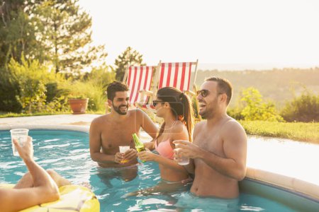 Gruppe von Freunden bei einem Sommerfest am Pool, Cocktails und Bier trinken und Spaß im Schwimmbad haben