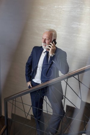 Photo for Senior businessman standing on modern office building staircase, having a phone conversation - Royalty Free Image