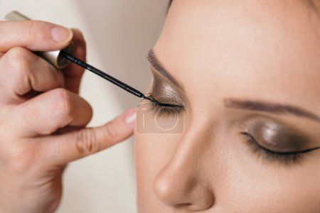 Téléchargez les photos : Artiste maquilleuse travaillant dans un studio de maquillage, mettant de l'eye-liner sur les paupières d'une cliente - en image libre de droit