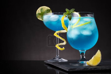 Téléchargez les photos : Cocktails lagon bleu avec liqueur de curaçao bleu, vodka, jus de citron et soda, décorés de tranches de citron et de feuilles de menthe. Focus sélectif sur les feuilles de menthe - en image libre de droit