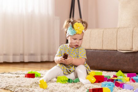 Foto de Hermosa niña, sentada en una alfombra en el piso del vivero, jugando con bloques de juguetes, pensativo y serio - Imagen libre de derechos