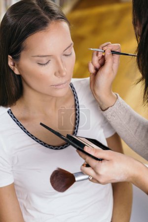 Téléchargez les photos : Maquilleuse travaillant dans un atelier de maquillage, appliquant les ombres à sourcils aux sourcils des clientes - en image libre de droit