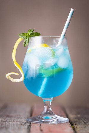 Téléchargez les photos : Cocktail lagon bleu avec liqueur de curaçao bleu, vodka, jus de citron et soda, décoré de tranches de citron et de feuilles de menthe sur une table en bois rustique - en image libre de droit