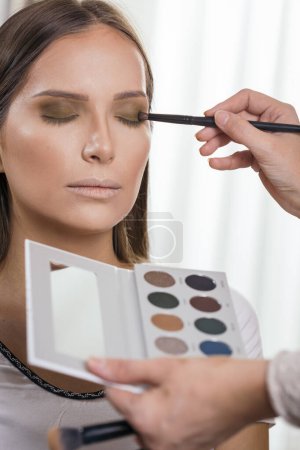 Téléchargez les photos : Maquilleuse travaillant dans un atelier de maquillage, ombrageant les paupières de la cliente - en image libre de droit