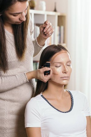 Photo for Make up artist applying face powder and corrector foundation to a female client's face, contouring the face - Royalty Free Image
