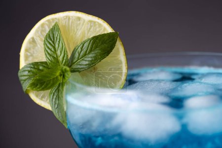 Photo for Detail of blue lagoon cocktail with blue curacao liqueur, vodka, lemon juice and soda, decorated with lemon slice and mint leaves. Selective focus on the mint leaves - Royalty Free Image