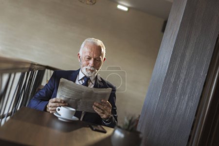 Téléchargez les photos : Homme d'affaires principal assis dans un restaurant moderne, buvant du café et lisant des journaux - en image libre de droit