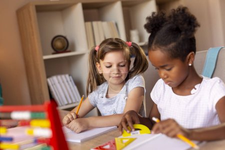 Foto de Dos niñas sentadas en un escritorio, escribiendo en sus cuadernos, haciendo una tarea de matemáticas y estudiando para la escuela - Imagen libre de derechos