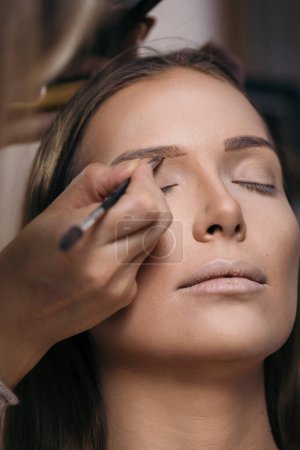 Téléchargez les photos : Maquilleuse travaillant dans un atelier de maquillage, appliquant les ombres à sourcils aux sourcils des clientes - en image libre de droit