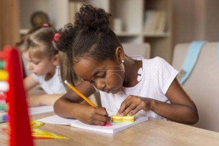 Photo for Two little girls sitting at a desk, writing in their notebooks, doing a math homework and studying for school - Royalty Free Image