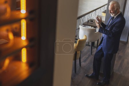 Téléchargez les photos : Homme d'affaires senior travaillant dans un hall d'entrée moderne d'immeuble de bureaux, en utilisant une tablette informatique - en image libre de droit