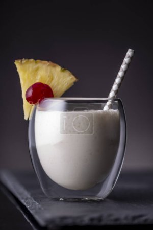 Photo for Pina colada cocktail with dark rum, pineapple juice and coconut cream served with drinking straw on a black stone tray - Royalty Free Image