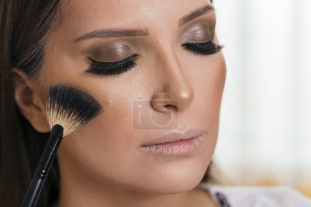 Téléchargez les photos : Maquilleuse travaillant dans un studio de maquillage, appliquant les surligneurs sur le visage de la cliente - en image libre de droit