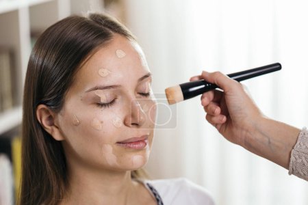 Foto de Maquillaje artista aplicando base de polvo de cara líquida a la cara de un cliente femenino con un cepillo de maquillaje - Imagen libre de derechos