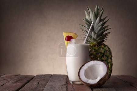 Téléchargez les photos : Verre de cocktail pina colada au rhum foncé, jus d'ananas et crème de coco, décoré de tranches d'ananas et de cerise marasquin sur table rustique en bois - en image libre de droit