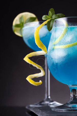 Téléchargez les photos : Cocktails lagon bleu avec liqueur de curaçao bleu, vodka, jus de citron et soda, décorés de tranches de citron et de feuilles de menthe. Focus sélectif sur les feuilles de menthe - en image libre de droit