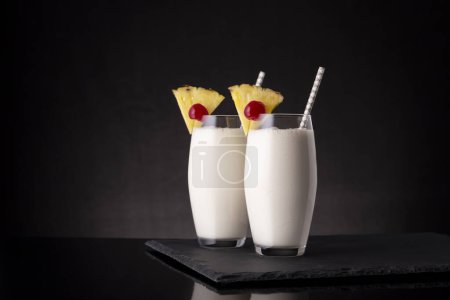 Photo for Two glasses of pina colada cocktail with dark rum, pineapple juice and coconut cream, decorated with pineapple slices and maraschino cherry - Royalty Free Image